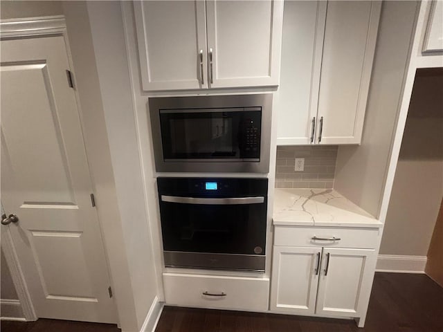 kitchen with white cabinets, stainless steel oven, built in microwave, and light stone countertops