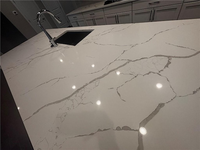 interior details with gray cabinets, sink, and light stone countertops