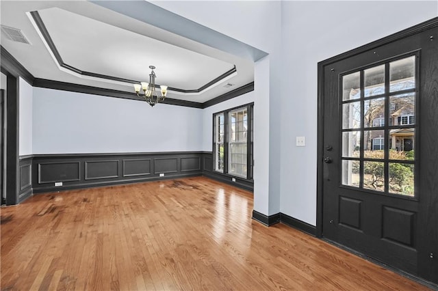 foyer entrance featuring visible vents, a raised ceiling, wainscoting, light wood-type flooring, and a chandelier