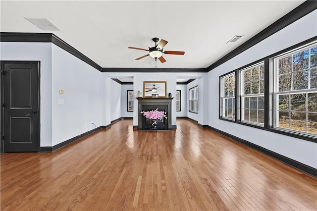 unfurnished living room featuring a wealth of natural light, a fireplace, ornamental molding, and wood finished floors