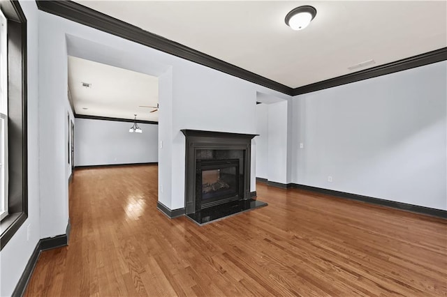 unfurnished living room featuring ceiling fan, wood finished floors, baseboards, ornamental molding, and a glass covered fireplace