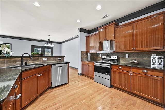 kitchen with a sink, visible vents, ornamental molding, wall chimney range hood, and appliances with stainless steel finishes