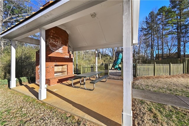 view of patio with an outdoor brick fireplace, a playground, and fence