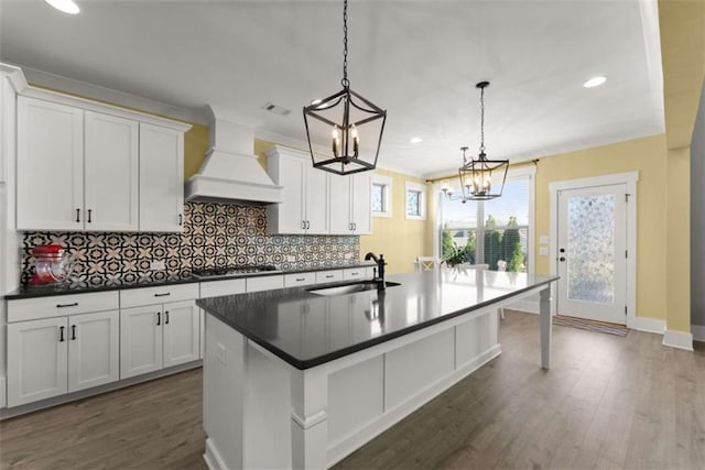 kitchen featuring custom exhaust hood, dark countertops, a sink, an island with sink, and gas cooktop