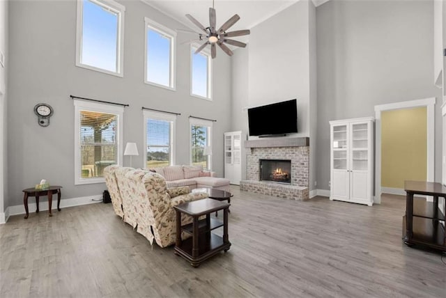 living area featuring ceiling fan, a fireplace, baseboards, and wood finished floors