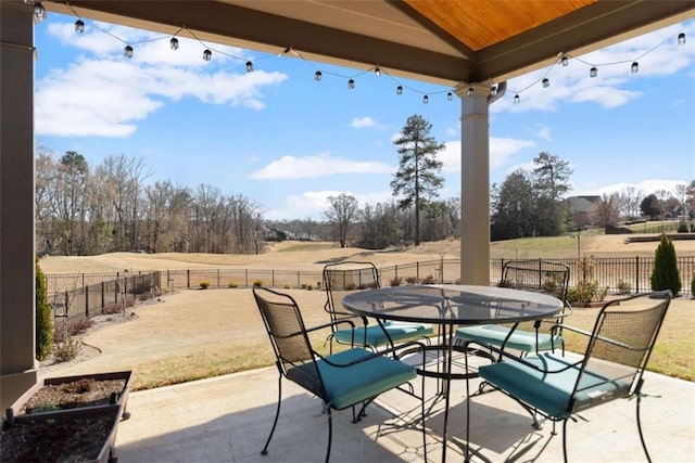 view of patio with outdoor dining area, a rural view, and fence