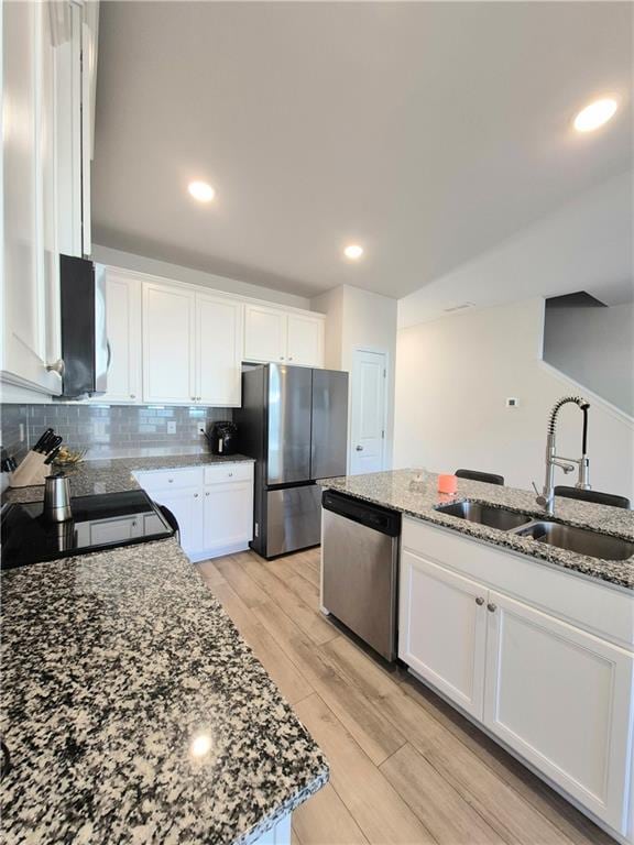 kitchen with light stone countertops, white cabinetry, sink, stainless steel appliances, and light hardwood / wood-style flooring