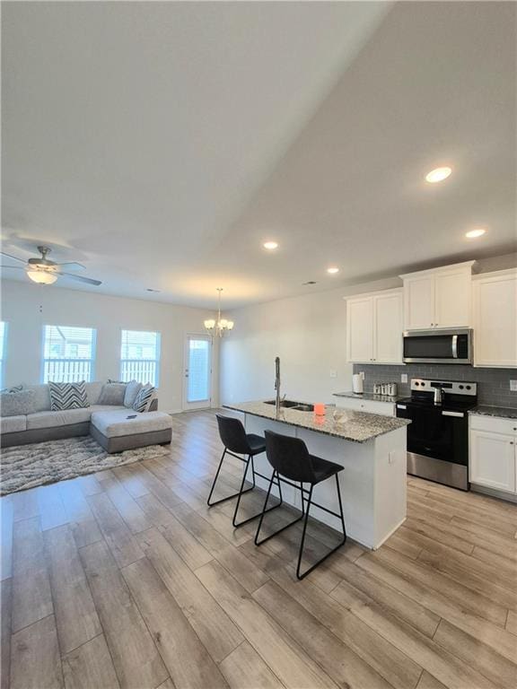 kitchen with white cabinets, an island with sink, appliances with stainless steel finishes, light hardwood / wood-style floors, and a kitchen bar