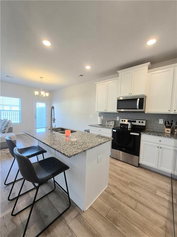 kitchen featuring white cabinetry, sink, stainless steel appliances, a kitchen island with sink, and light wood-type flooring