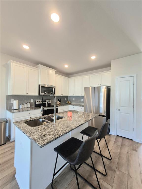 kitchen with light stone counters, light hardwood / wood-style flooring, white cabinets, and appliances with stainless steel finishes