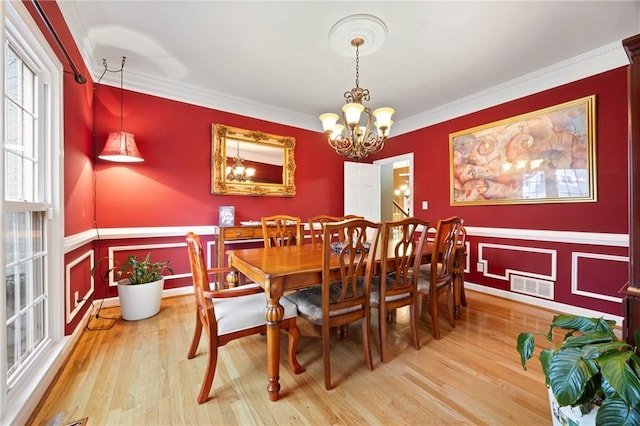 dining room with ornamental molding, light wood-type flooring, visible vents, and a notable chandelier