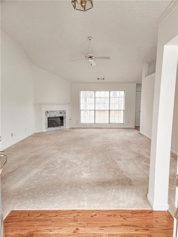 unfurnished living room featuring a premium fireplace, ornamental molding, light carpet, and ceiling fan