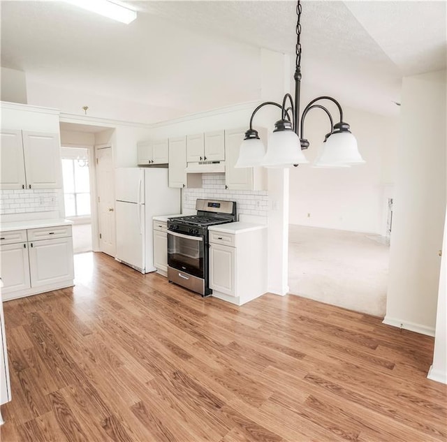 kitchen with stainless steel gas stove, white cabinets, decorative backsplash, hanging light fixtures, and white fridge