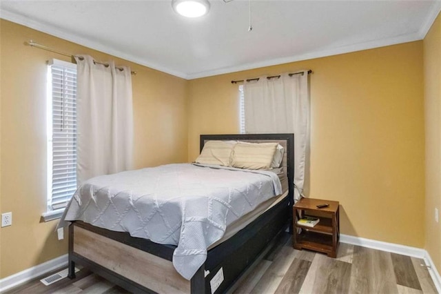 bedroom featuring visible vents, ornamental molding, baseboards, and wood finished floors