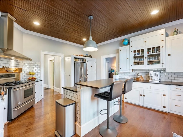 kitchen featuring white cabinetry, wall chimney exhaust hood, decorative light fixtures, and appliances with stainless steel finishes