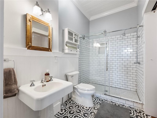 bathroom featuring sink, toilet, wooden walls, a shower with shower door, and ornamental molding