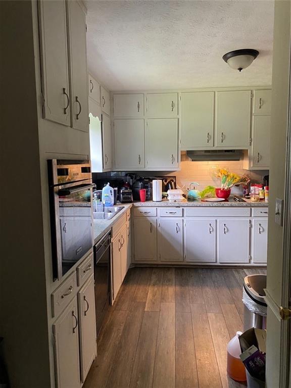 kitchen featuring dishwasher, dark wood-type flooring, stainless steel oven, and white cabinetry