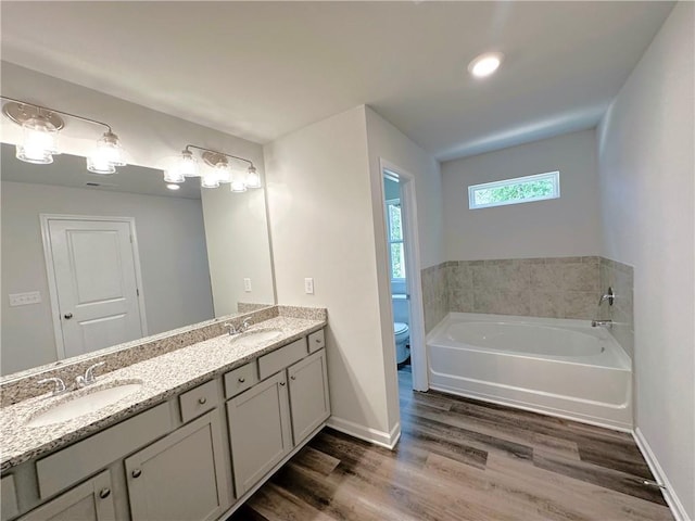 bathroom featuring toilet, wood finished floors, a sink, a bath, and double vanity