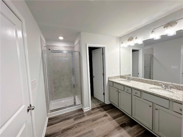 bathroom with a stall shower, double vanity, a sink, and wood finished floors