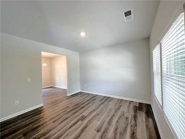 spare room featuring dark wood-type flooring, visible vents, and baseboards