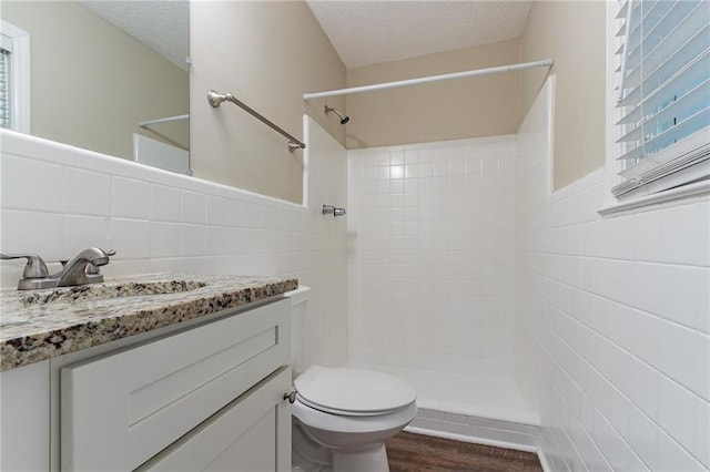 bathroom with tiled shower, toilet, vanity, hardwood / wood-style floors, and tile walls