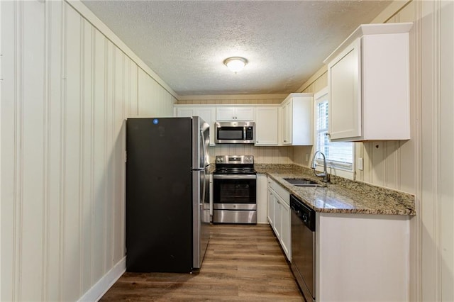 kitchen with stainless steel appliances, sink, white cabinetry, light stone counters, and dark hardwood / wood-style flooring