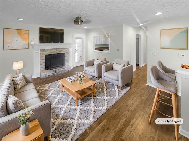 living room with a textured ceiling, a brick fireplace, hardwood / wood-style flooring, and ceiling fan