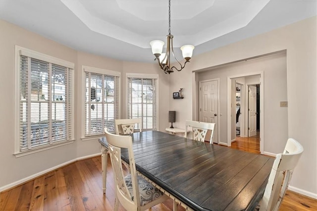 dining space featuring a raised ceiling, baseboards, wood-type flooring, and a chandelier