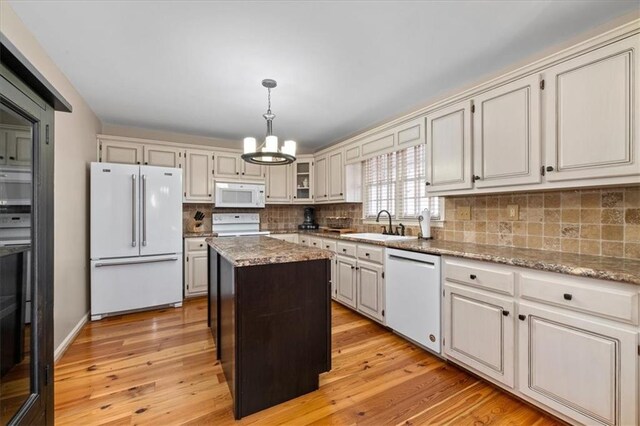 kitchen with a sink, a kitchen island, tasteful backsplash, white appliances, and an inviting chandelier