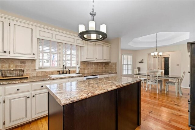 kitchen with light wood-style flooring, a sink, decorative backsplash, a raised ceiling, and a chandelier