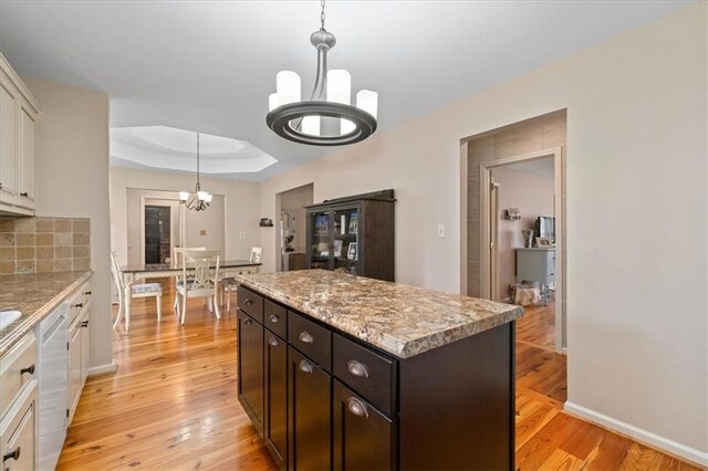 kitchen featuring a chandelier, light wood finished floors, tasteful backsplash, and a raised ceiling