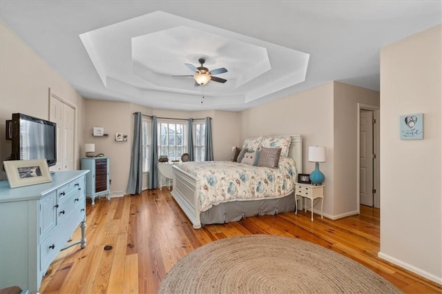 bedroom with light wood finished floors, a ceiling fan, a raised ceiling, and baseboards