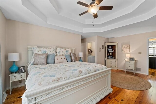 bedroom with visible vents, a tray ceiling, wood finished floors, baseboards, and ceiling fan