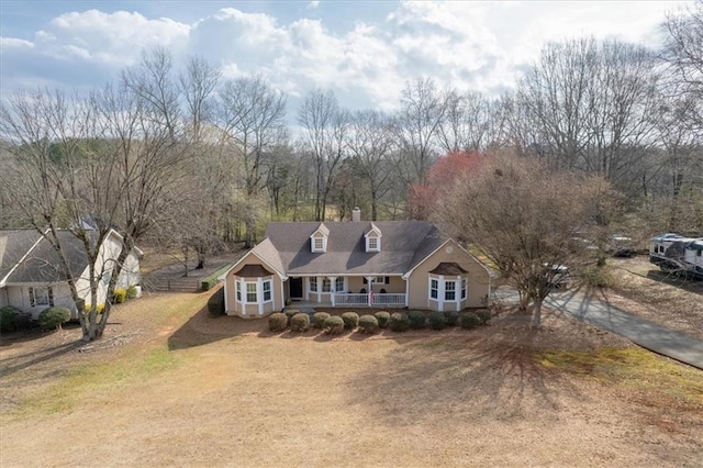 new england style home with a front lawn, covered porch, and a chimney