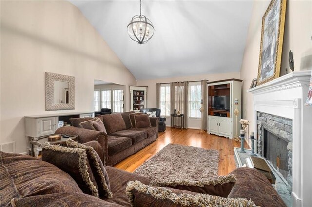 living room with a notable chandelier, light wood-style flooring, a fireplace, and high vaulted ceiling