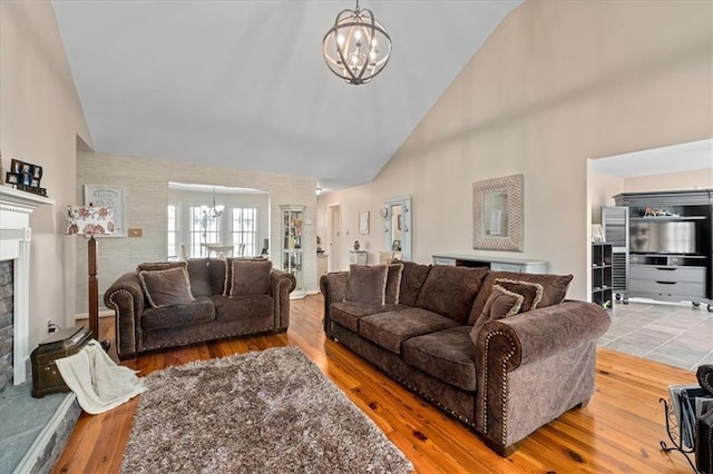 living area with a fireplace with raised hearth, a notable chandelier, wood finished floors, and high vaulted ceiling