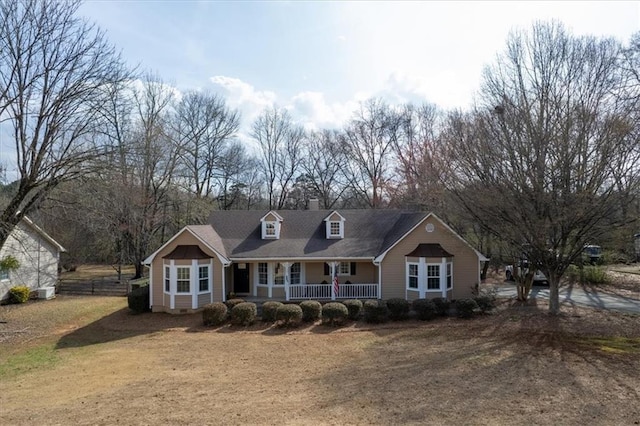 cape cod home with a front lawn, covered porch, and a chimney