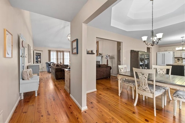 dining area with baseboards, light wood-style floors, an inviting chandelier, and a raised ceiling