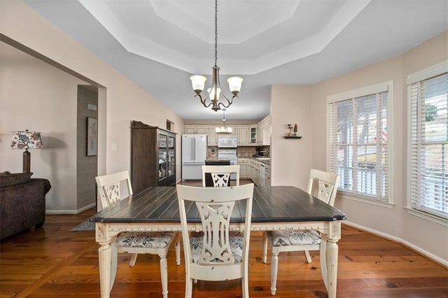 dining room featuring a notable chandelier, baseboards, a tray ceiling, and wood finished floors