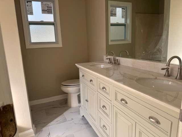 full bathroom featuring marble finish floor, double vanity, a sink, and baseboards