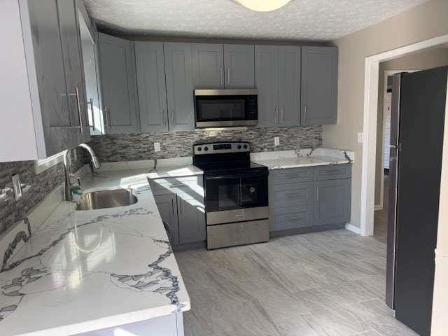 kitchen featuring decorative backsplash, appliances with stainless steel finishes, light stone countertops, gray cabinetry, and a sink