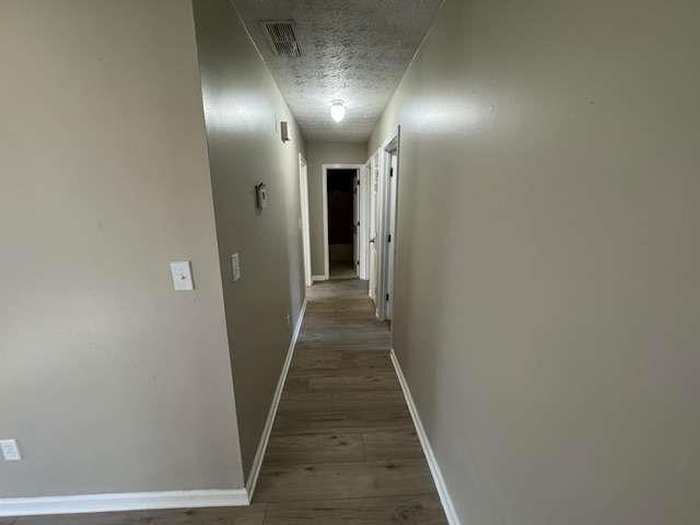 hall featuring dark wood-style floors, baseboards, visible vents, and a textured ceiling