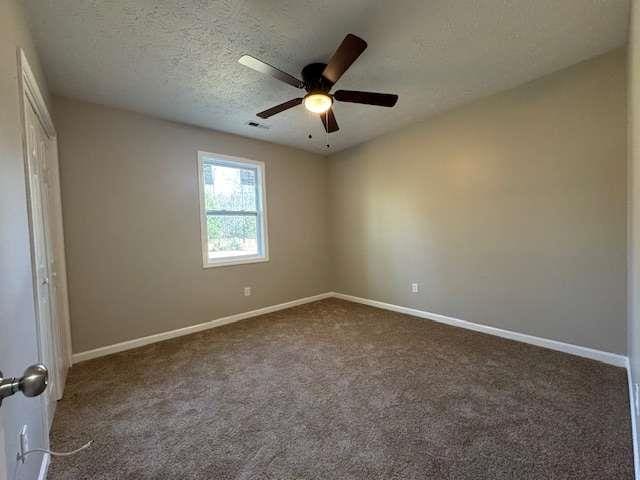 empty room featuring a textured ceiling, dark carpet, a ceiling fan, and baseboards