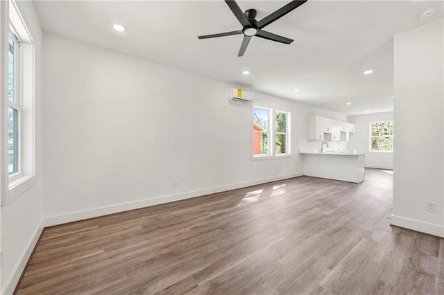 unfurnished living room featuring recessed lighting, baseboards, a wall unit AC, and wood finished floors