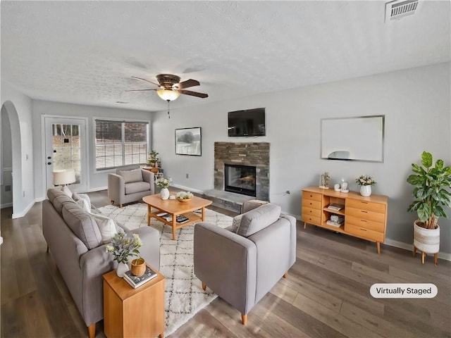 living room featuring a stone fireplace, ceiling fan, hardwood / wood-style floors, and a textured ceiling