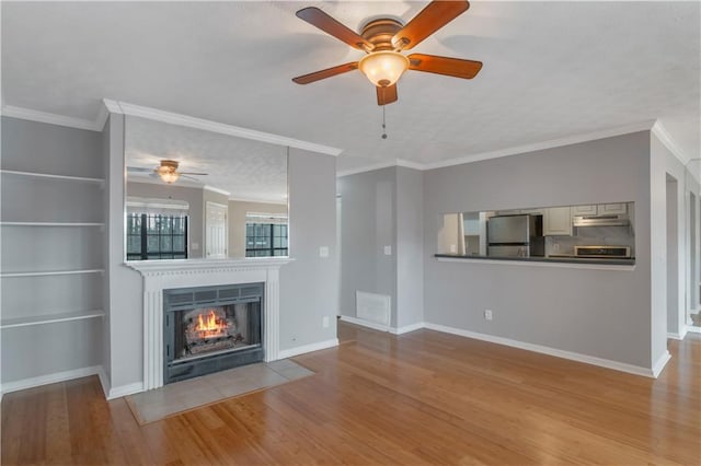 unfurnished living room with ornamental molding, built in shelves, ceiling fan, and light hardwood / wood-style flooring