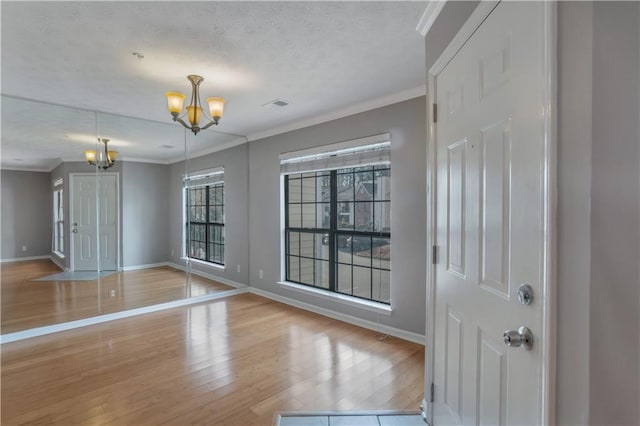 spare room with ornamental molding, an inviting chandelier, and light hardwood / wood-style floors