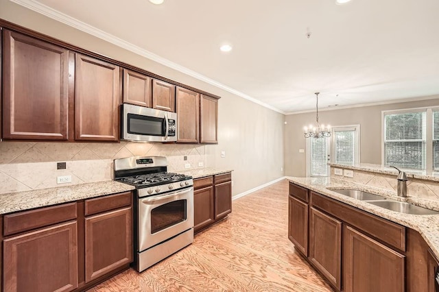 kitchen featuring sink, light wood-type flooring, light stone countertops, appliances with stainless steel finishes, and a notable chandelier