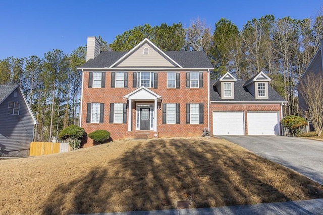 colonial-style house featuring brick siding, an attached garage, driveway, and fence