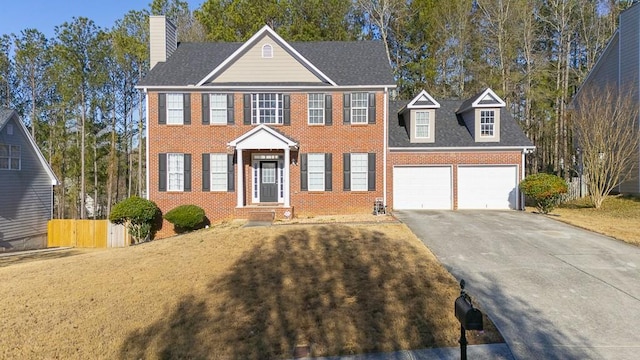 colonial home with brick siding, fence, aphalt driveway, a chimney, and a garage